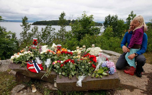 People mourn next to flowers in front of Utoeya island northwest of Oslo...People mourn next to flowers in front of Utoeya island, northwest of Oslo July 25, 2011. At least 93 people are dead after a gunman dressed in police uniform opened fire at a youth camp of Norway's ruling political party on Friday in Utoeya island, hours after a bomb blast in the government district in the capital Oslo. According to local media, four or five participants at the youth camp are still unaccounted for.   REUTERS/Fabrizio Bensch (NORWAY - Tags: CIVIL UNREST CRIME LAW)