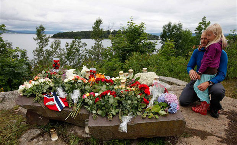 People mourn next to flowers in front of Utoeya island northwest of Oslo...People mourn next to flowers in front of Utoeya island, northwest of Oslo July 25, 2011. At least 93 people are dead after a gunman dressed in police uniform opened fire at a youth camp of Norway's ruling political party on Friday in Utoeya island, hours after a bomb blast in the government district in the capital Oslo. According to local media, four or five participants at the youth camp are still unaccounted for.   REUTERS/Fabrizio Bensch (NORWAY - Tags: CIVIL UNREST CRIME LAW)